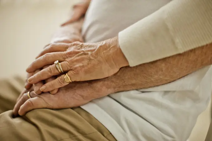 Hands of a senior couple resting on top of each other.