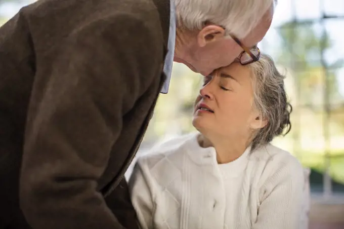 Elderly man kisses his wife on the forehead.