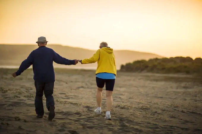 Elderly couple enjoy going for a walk together along the beach at sunset.