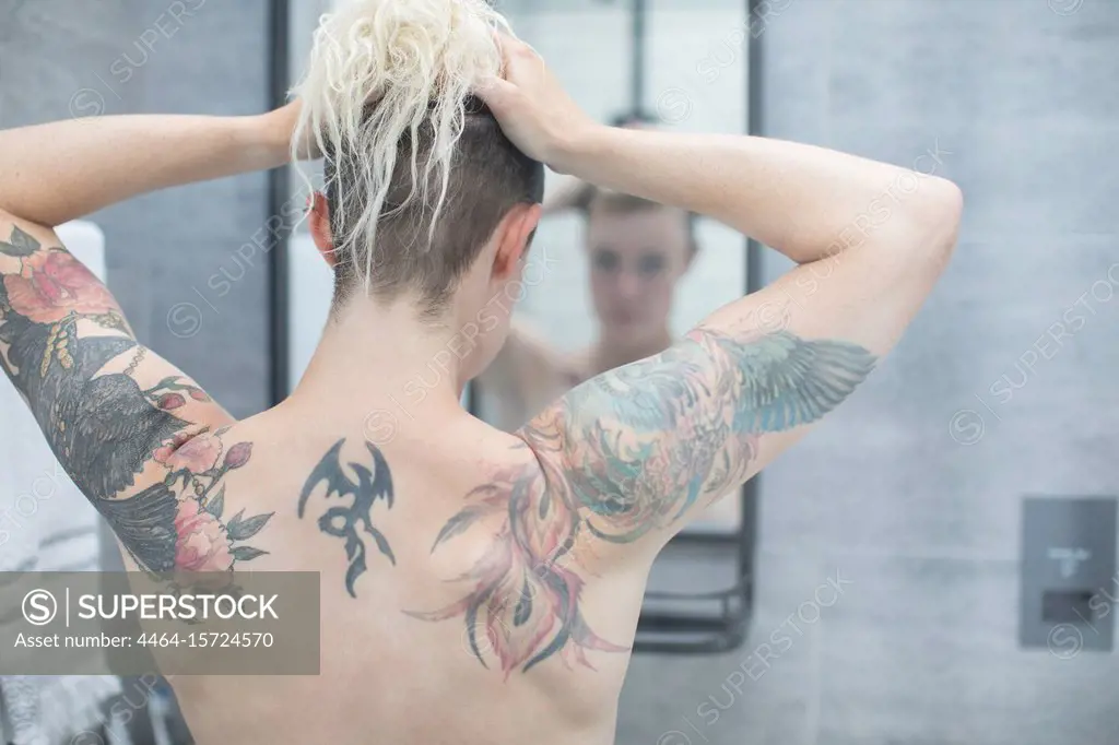 Woman with tattooed back at bathroom mirror