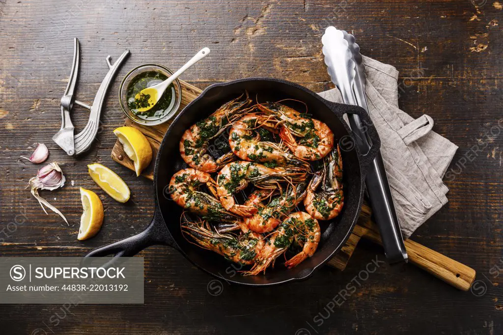 Tiger prawns shrimps roasted on frying grill pan with green sauce, lemon  and garlic on wooden background - SuperStock