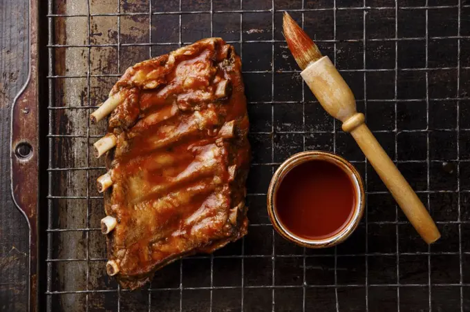 BBQ grilled smoked pork ribs and sauce brush on dark metal baking sheet background