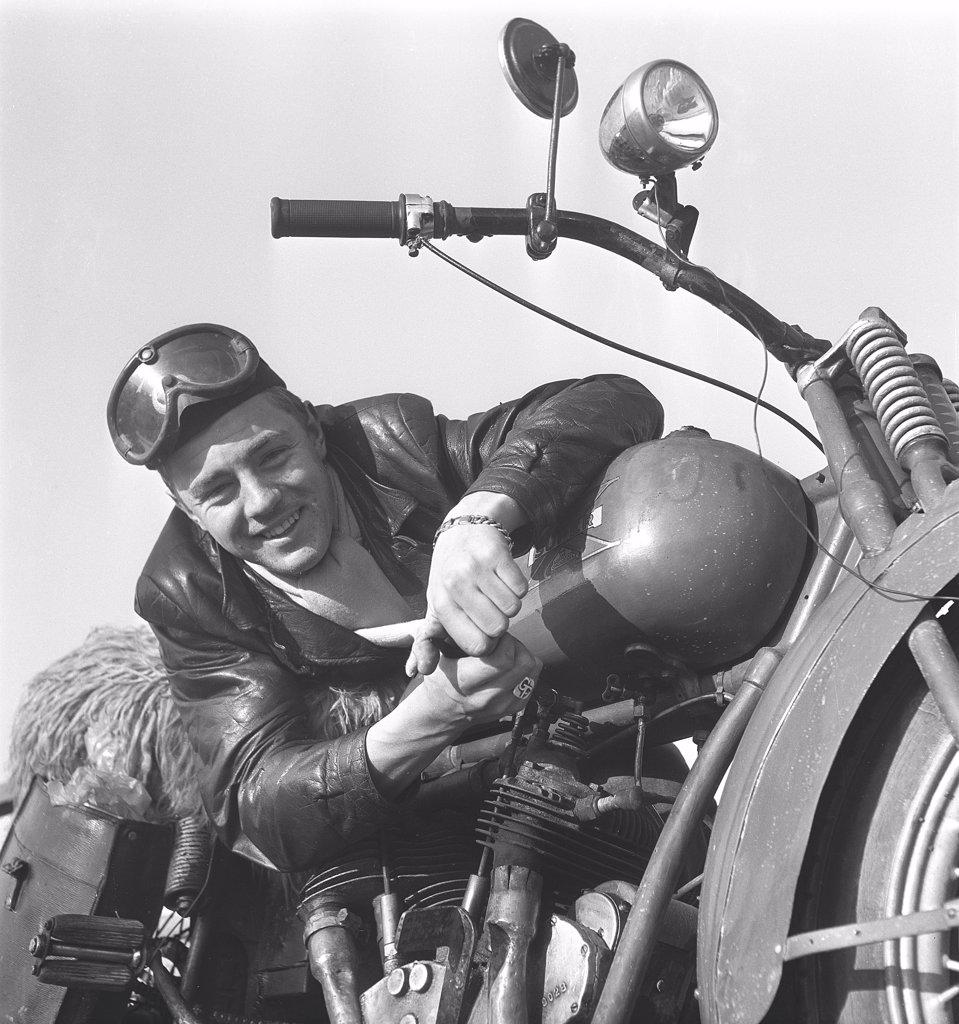 Motorcyclist in the 1950s. A young man wearing glasses and a leather cap by his motorcycle. The motorcycle is made by the american company Excelsior in Chicage and the model is Super X 1925, and was americas first motorcycle with a v-twin engine. Sweden 1950s ref 10-09-11