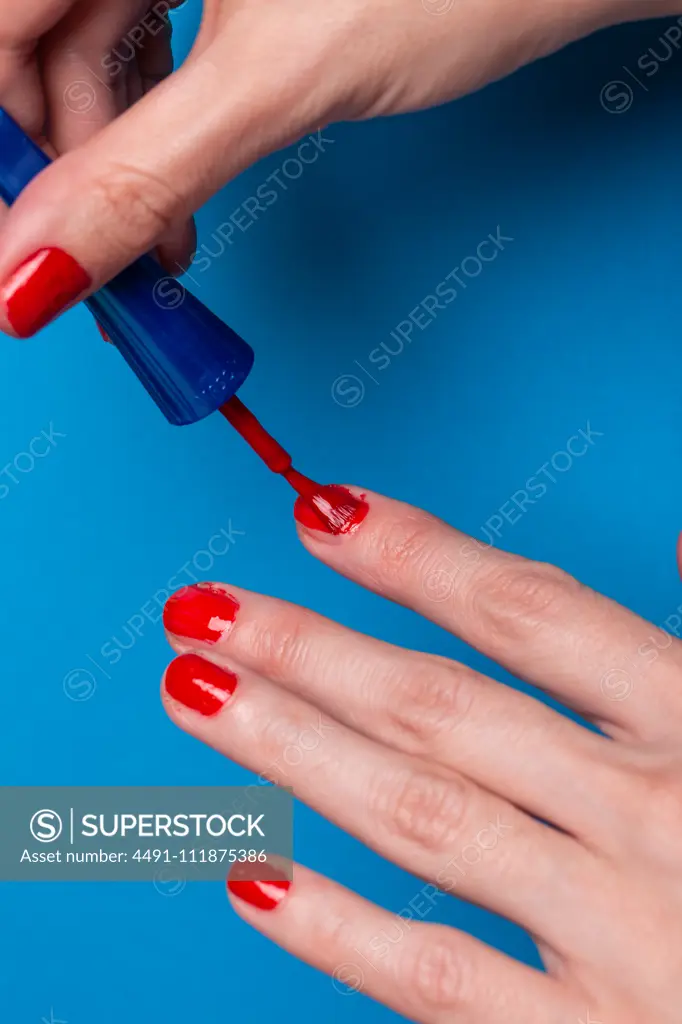 Unrecognizable female applying red lacquer on fingernails while doing  manicure against blue background - SuperStock