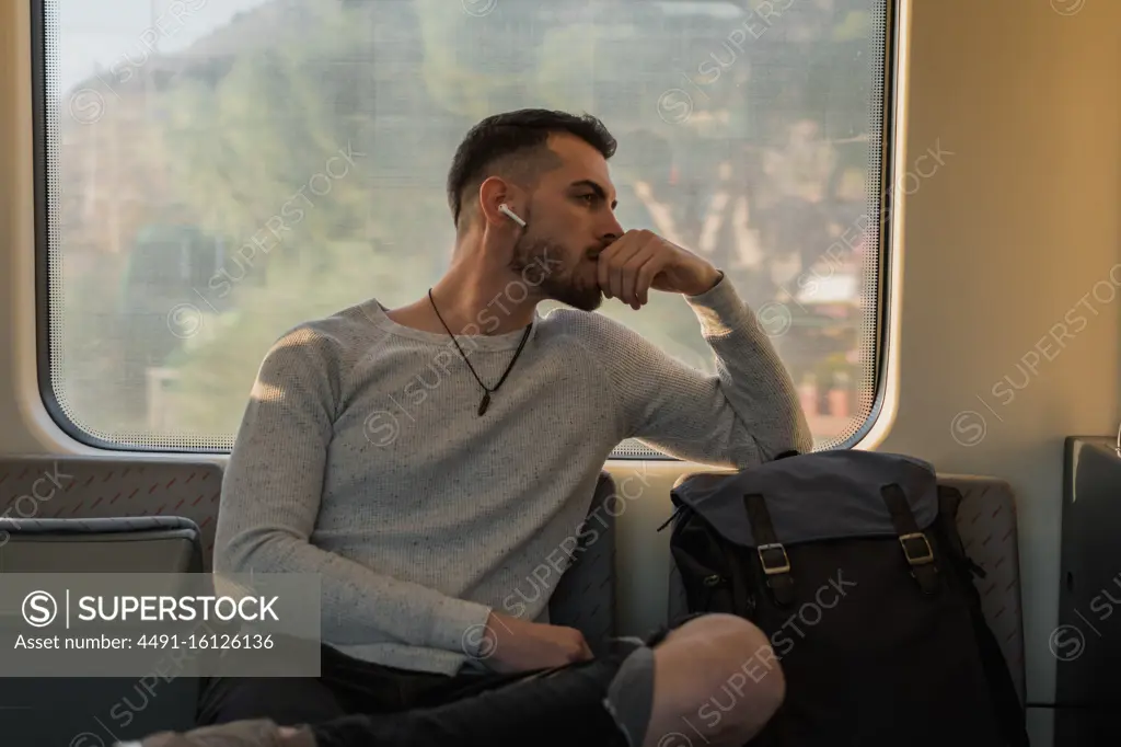 Thoughtful young male passenger listening to music in subway car