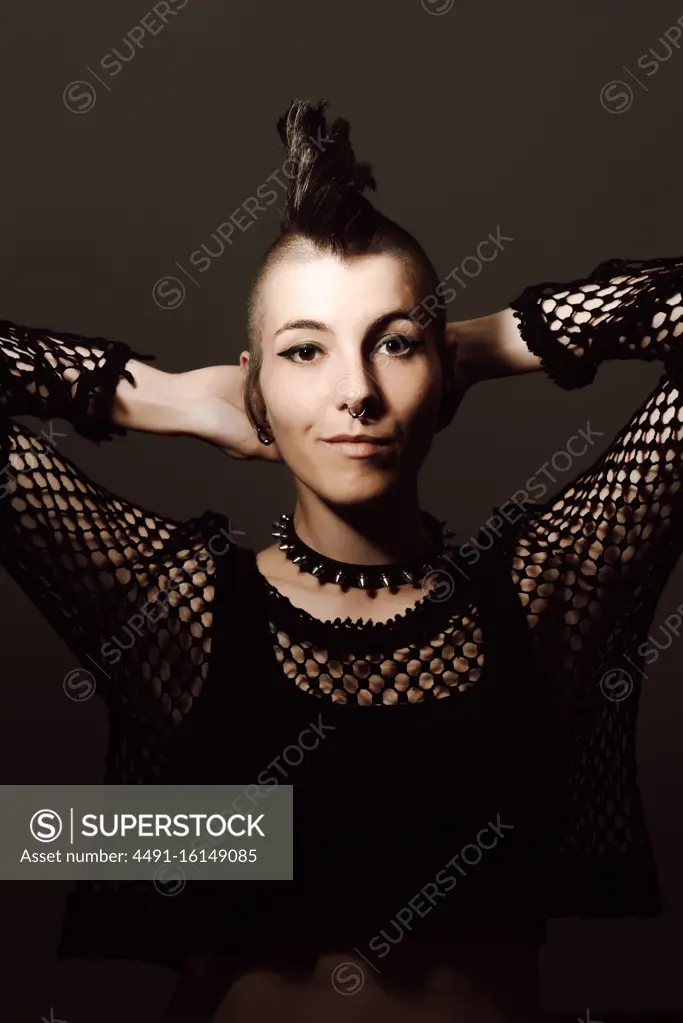 adult lady with mohawk looking at camera while standing against brown background