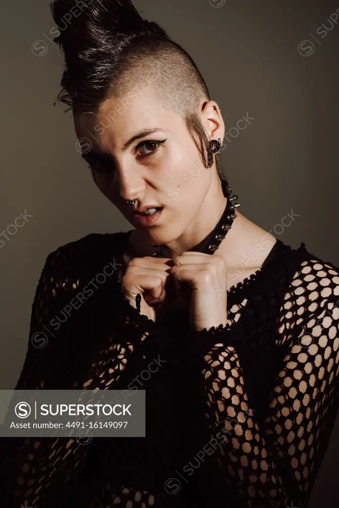 Serious adult lady with mohawk looking at camera while standing against brown background