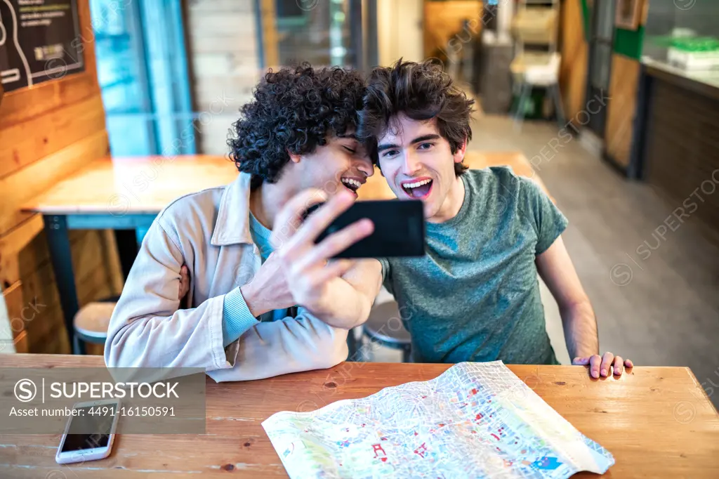 Multiethnic young homosexual men taking a selfie photo on smartphone and having fresh drinks smiling while sitting at cafe table during romantic date