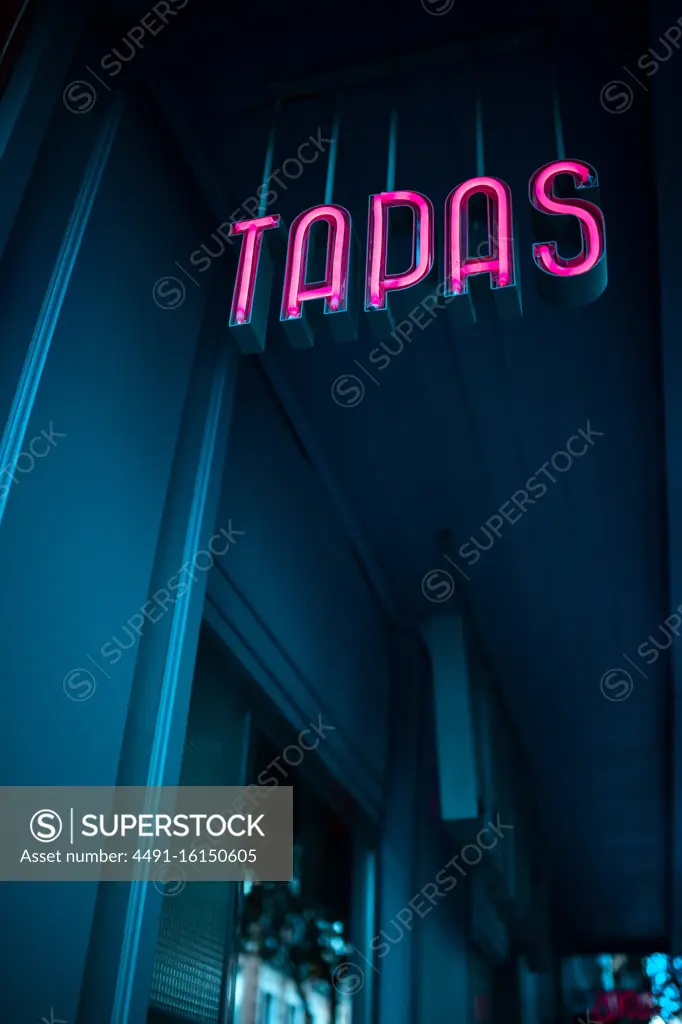 From below pink Tapas sign hanging outside diner in evening on town street