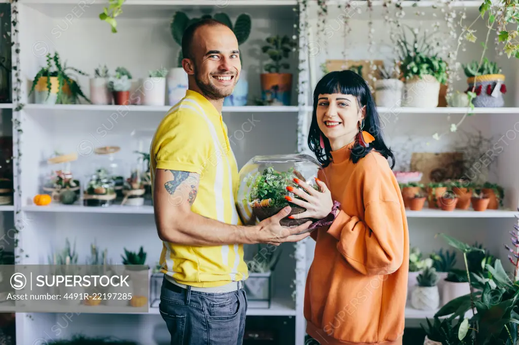 Man and woman holding plants in glass container. Flower shop, florist, small business, teamwork.