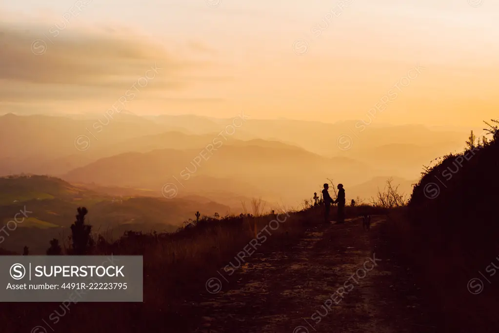 Side view of homosexual couple embracing near dog on route in darkness and picturesque view of valley in fog
