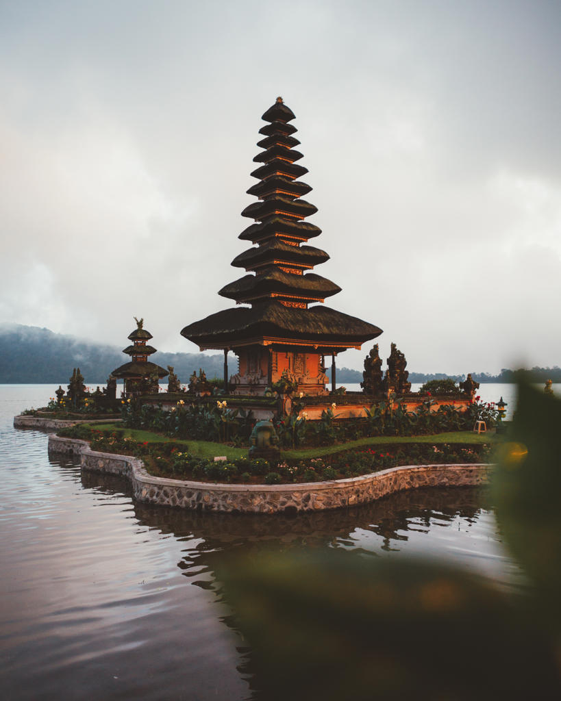 Small complex of prayer pagoda with green garden around built in water on shore against fog, Bali