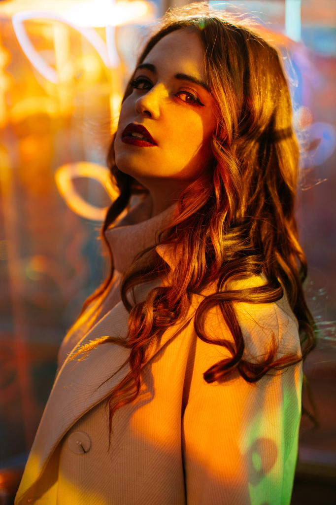 Sensual young woman in coat in light of neon signs