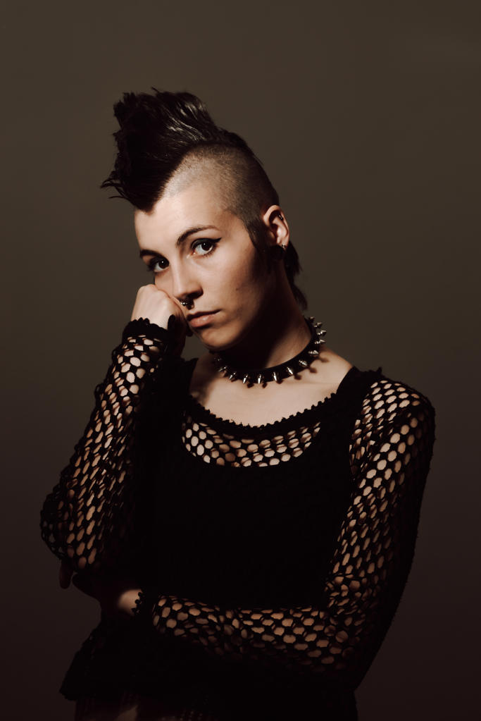 Serious adult lady with mohawk looking at camera while standing against brown background