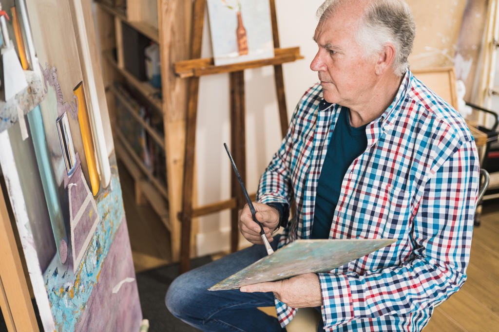 Aged man painting picture with brush