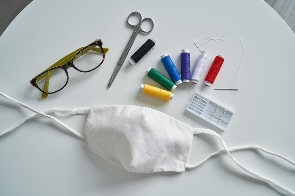 Top view of colorful threads and various instruments for medical mask sewing placed on table near glasses
