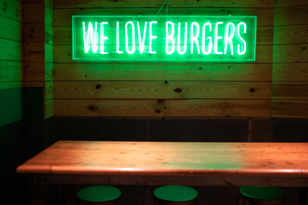 Bright green We love burgers sign glowing with neon light over wooden table in evening in modern cafeteria
