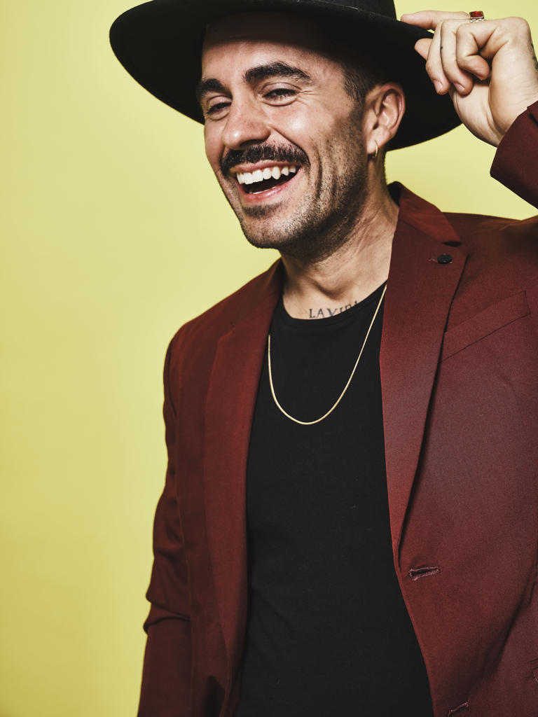 Laughing adult ethnic male in trendy vinous suit and hat looking at camera while standing against yellow background