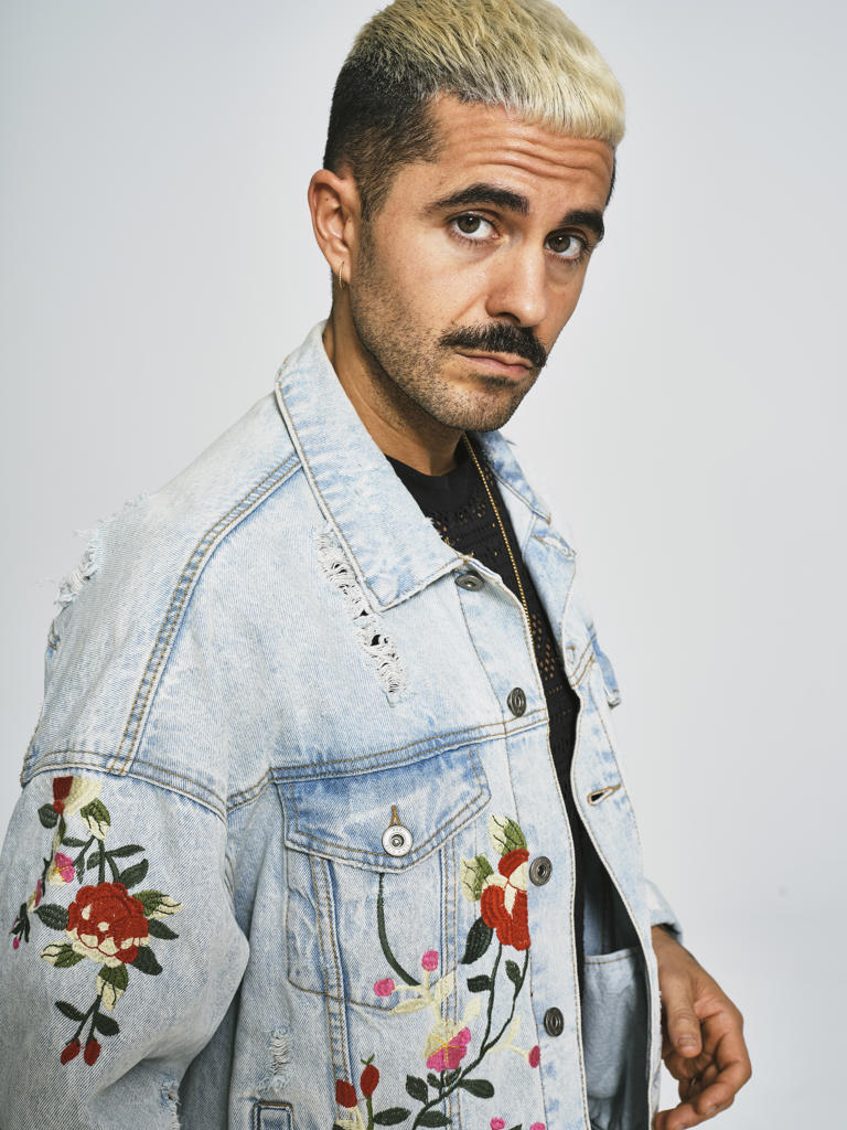 Portrait of young ethnic looking at camera wearing trendy denim jacket with floral pattern while standing against gray background
