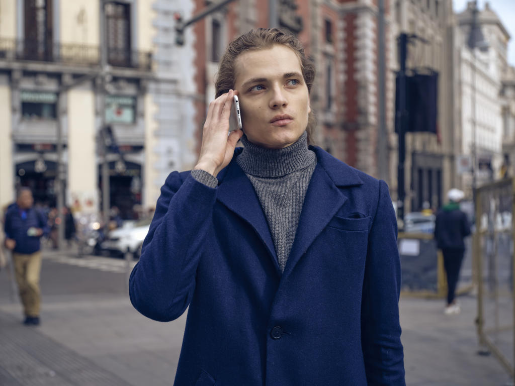 Modern elegant male in trendy coat looking away pensively while having phone conversation on city street