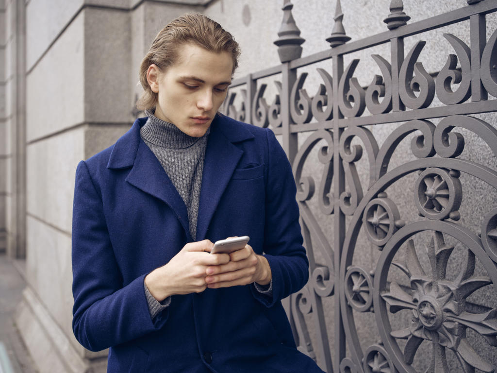 Stylish young man browsing on smartphone on street on city street
