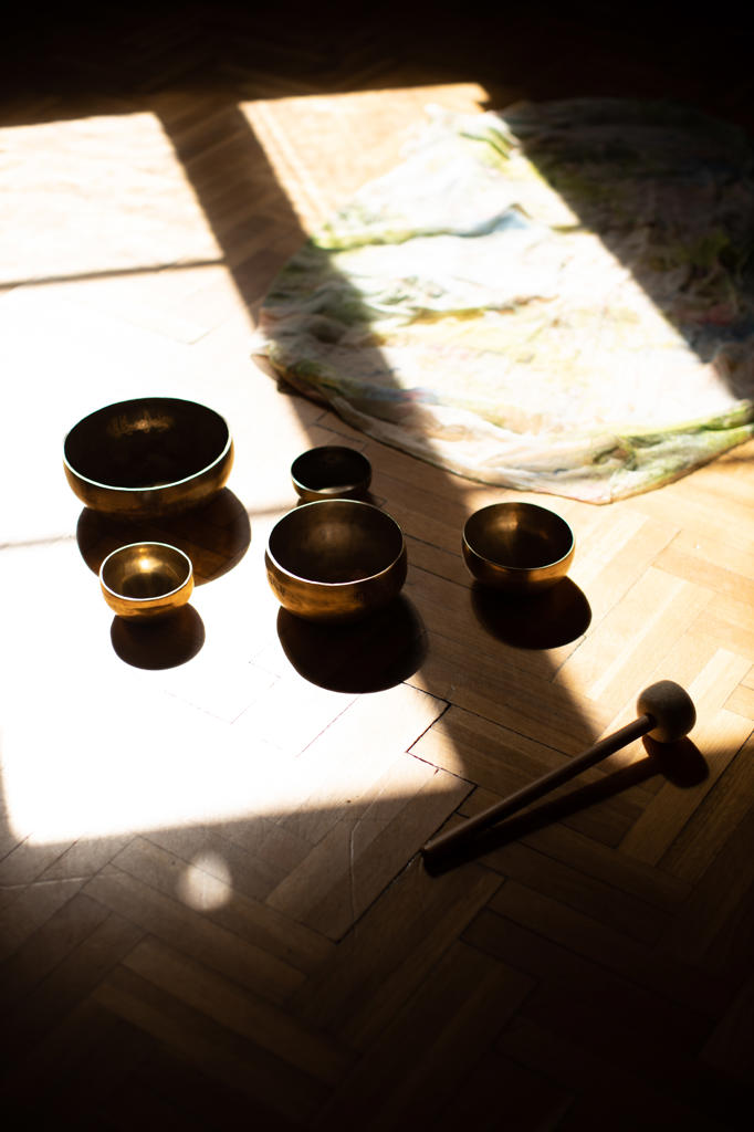 From above collection of traditional tibetan bowls and striker placed in sunlight on wooden floor in dark room