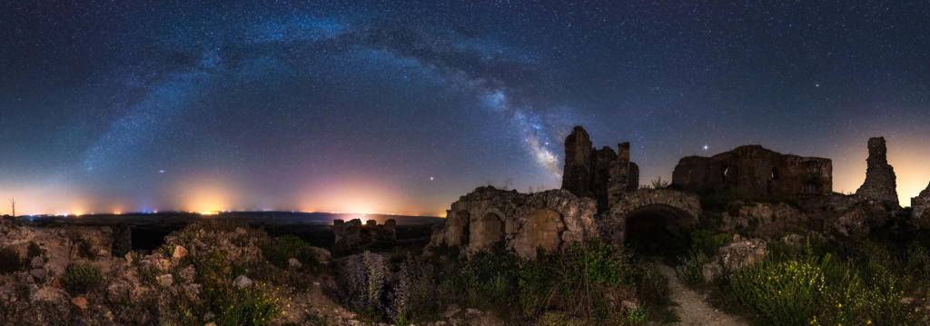 Aged ruined building among green field plants under colorful starry night sky with milky way