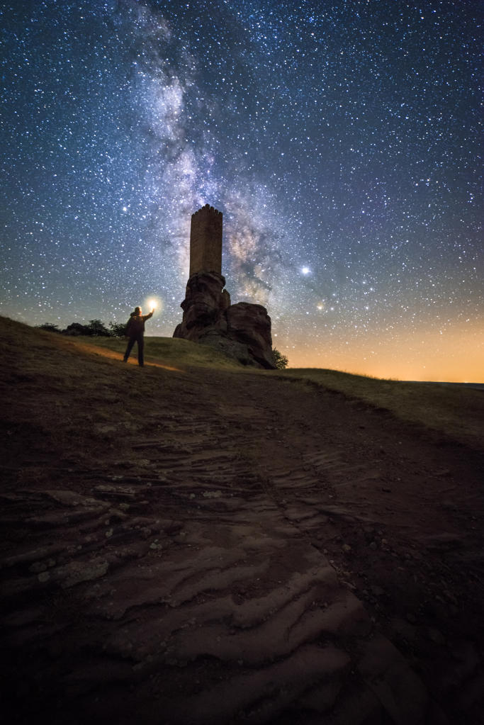 Back view of faceless traveler sightseeing remains of ancient castle under Milky Way at starry night with lantern light