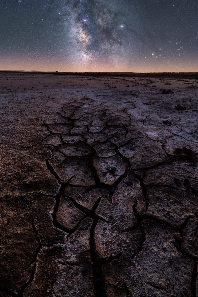 From above of dry cracked surface of ground and colorful night starry sky on horizon