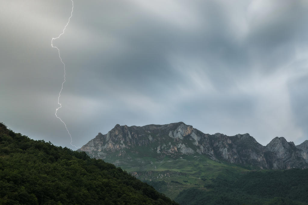 Majestic long exposure view of thin lightning striking mountain range against overcast sky on stormy day in nature