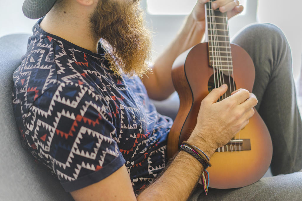 Bearded man sitting in armchair and playing guitar at home.