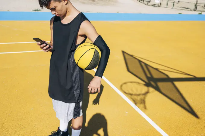 Male basketball player using his smartphone resting after training session. 