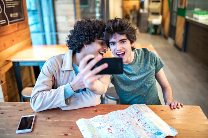 Multiethnic young homosexual men taking a selfie photo on smartphone and having fresh drinks smiling while sitting at cafe table during romantic date