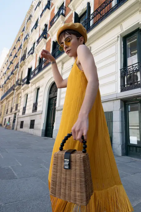 Low angle of slim young stylish woman in trendy yellow outfit waving skirt of dress while dancing on street on sunny day in Madrid