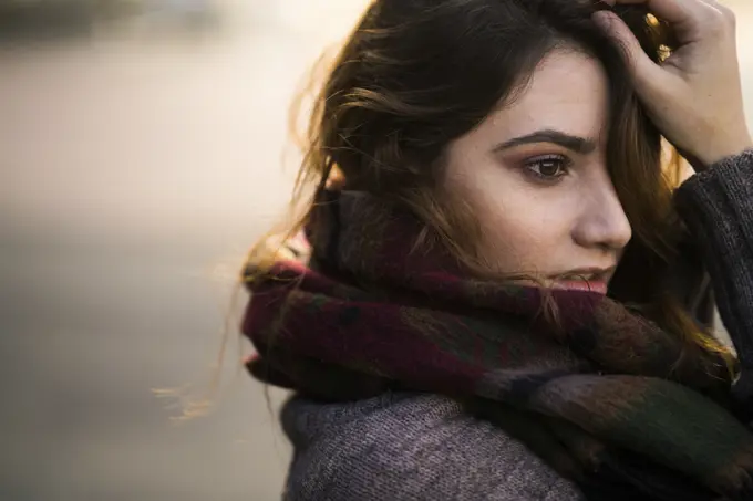 Portrait of young woman standing in warm clothes touching her face.