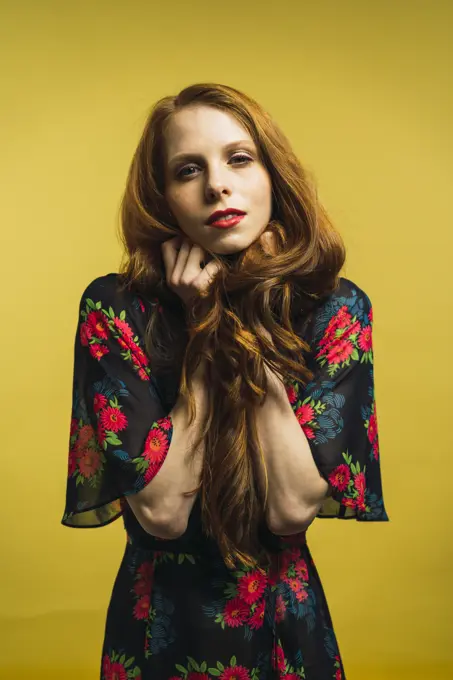 Portrait of pretty redhead woman holding hair and looking at camera on yellow background.