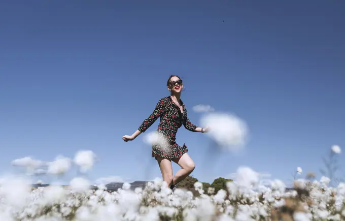 Attractive young woman in sunglasses standing on white field with flowers.