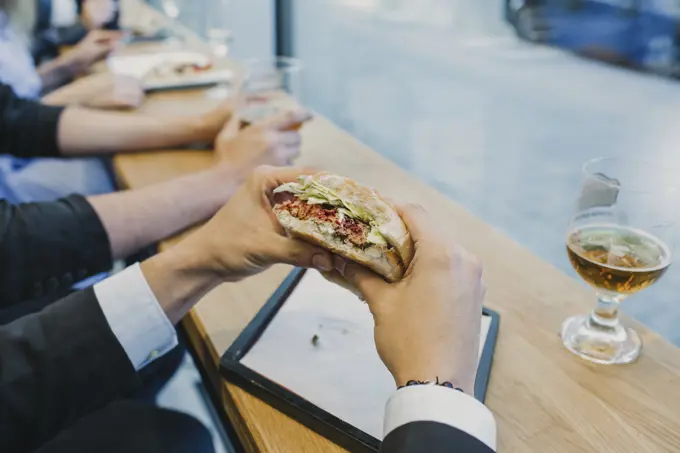 Hand of unrecognizable man in suit holding tasty burger in cafe.