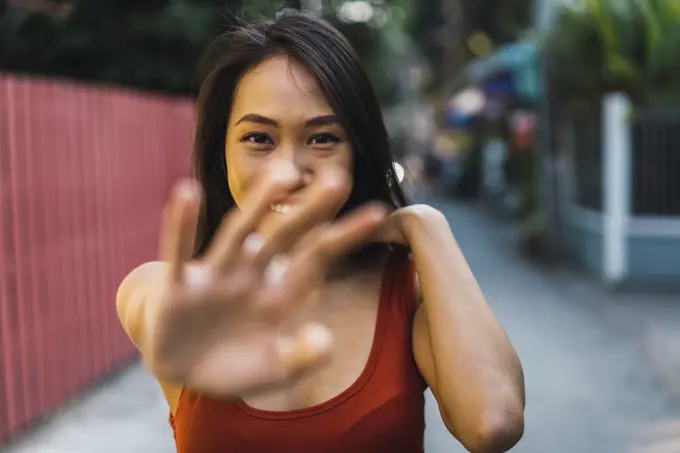 Cheerful Asian woman closing face and gesturing stop on town street.