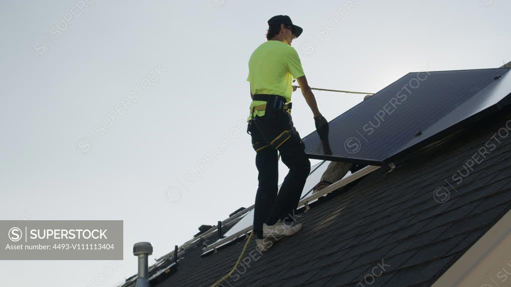Medium Panning Low Angle Shot Of Workers Installing Solar Panel On Roof 