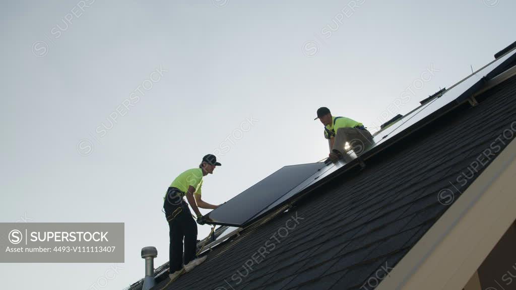 wide-panning-low-angle-shot-of-workers-installing-solar-panel-on-roof