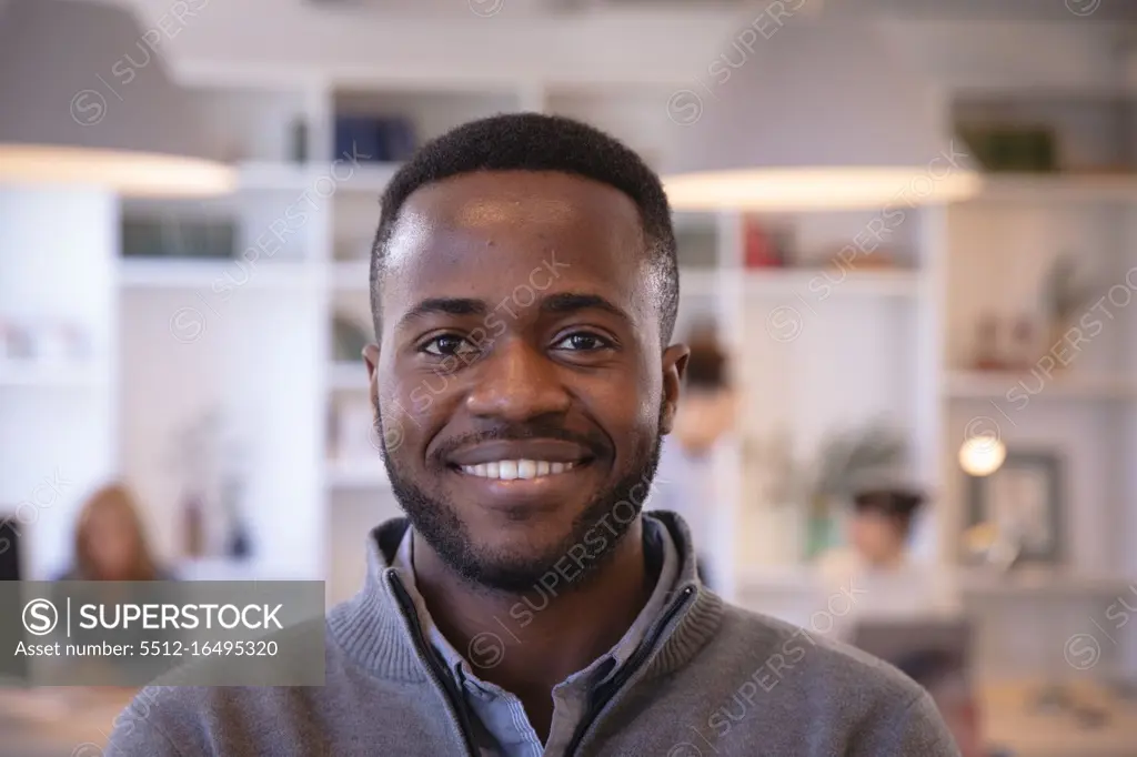 Portrait of a happy African American businessman working in a modern office, looking at camera and smiling, with his colleagues working in the background