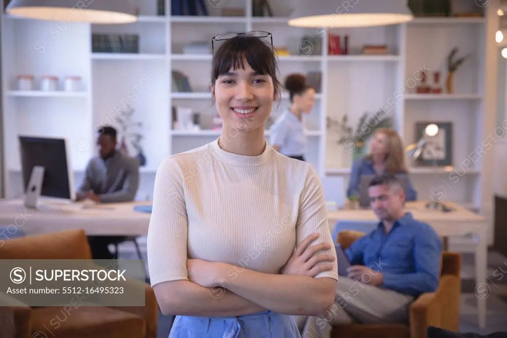 Portrait of a happy Asian businesswoman working in a modern office, looking at camera and smiling, with her colleagues working in the background