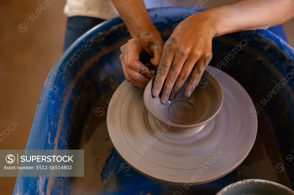 Elevated close up of the hands of a young Caucasian female potter shaping wet clay into a bowl shape on a potters wheel in a pottery studio