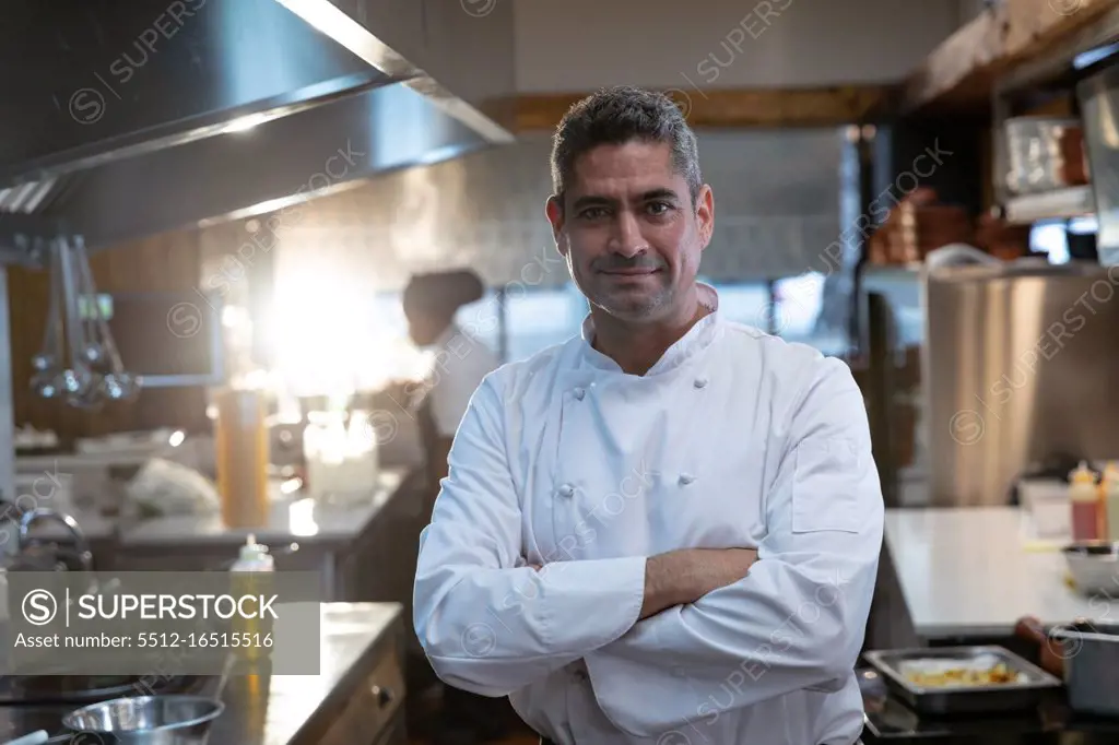 Portrait close up of a smiling middle aged Caucasian male chef wearing whites standing with arms crossed in a restaurant kitchen
