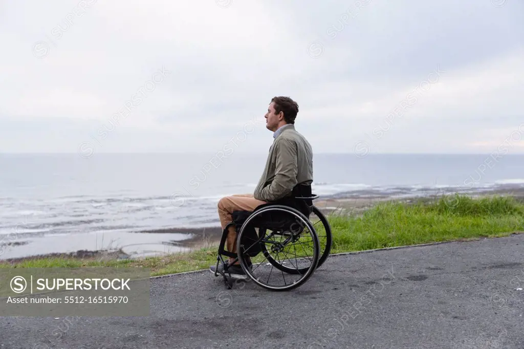 Side view of a young Caucasian man in a wheelchair enjoying a day out by the sea, enjoying the view
