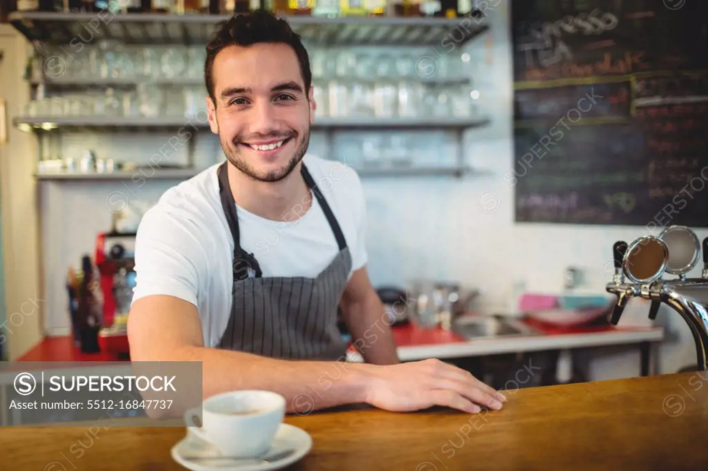 Portrait of confident young waiter with coffee at counter in cafeteria