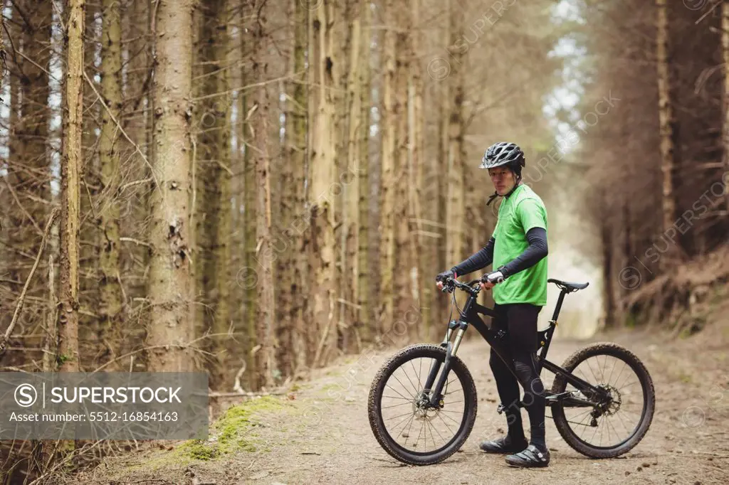 Side view of mountain biker standing by trees in forest