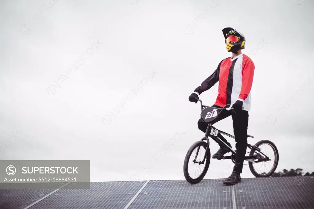 Cyclist standing with BMX bike on starting ramp at skatepark