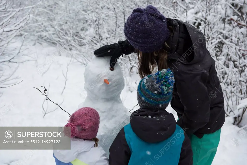 Mother with children making snowman on beautiful snowy day